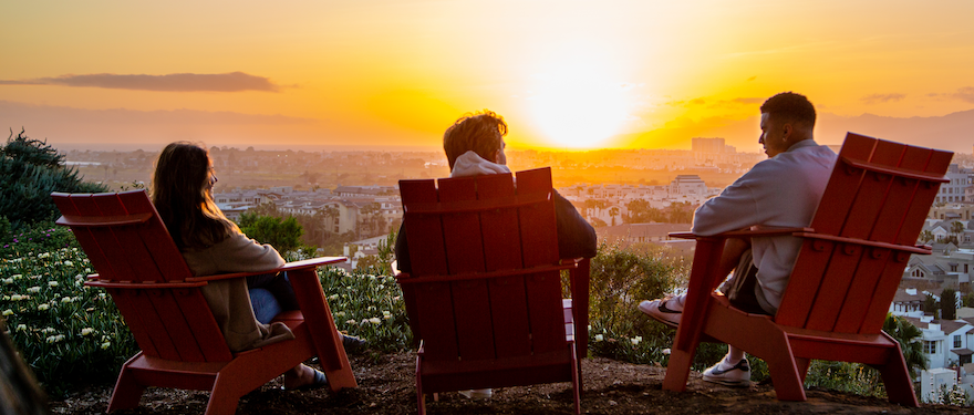 Three students sitting near the bluff, looking at the sunset.